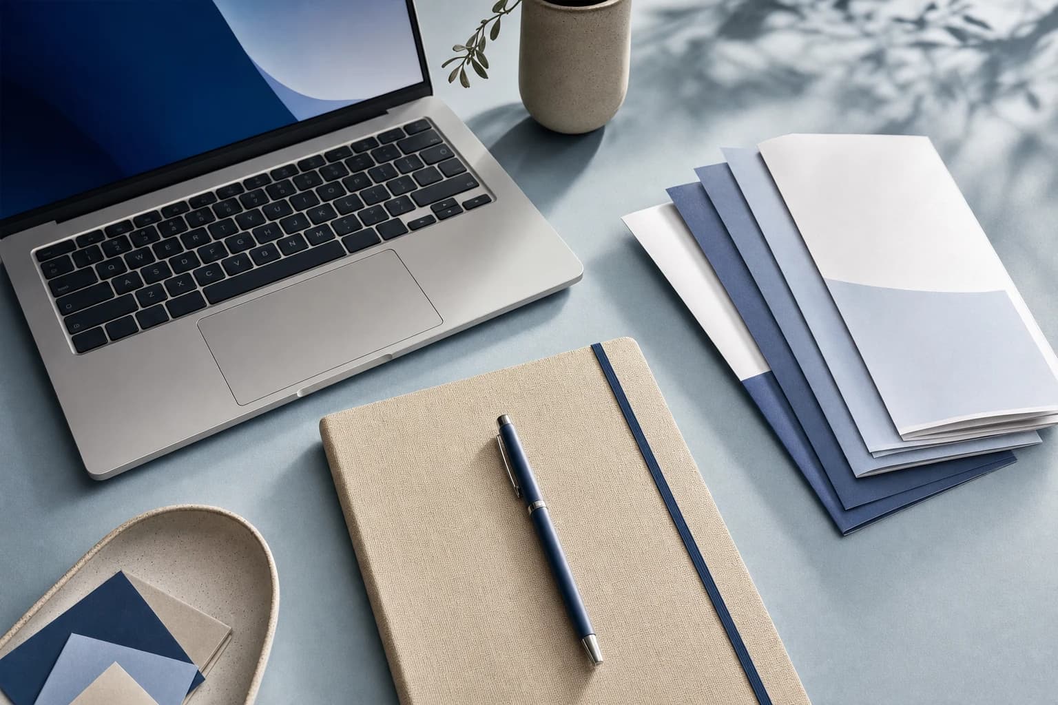 Notebook und Unterlagen neben einem Laptop auf einem hellen Schreibtisch.